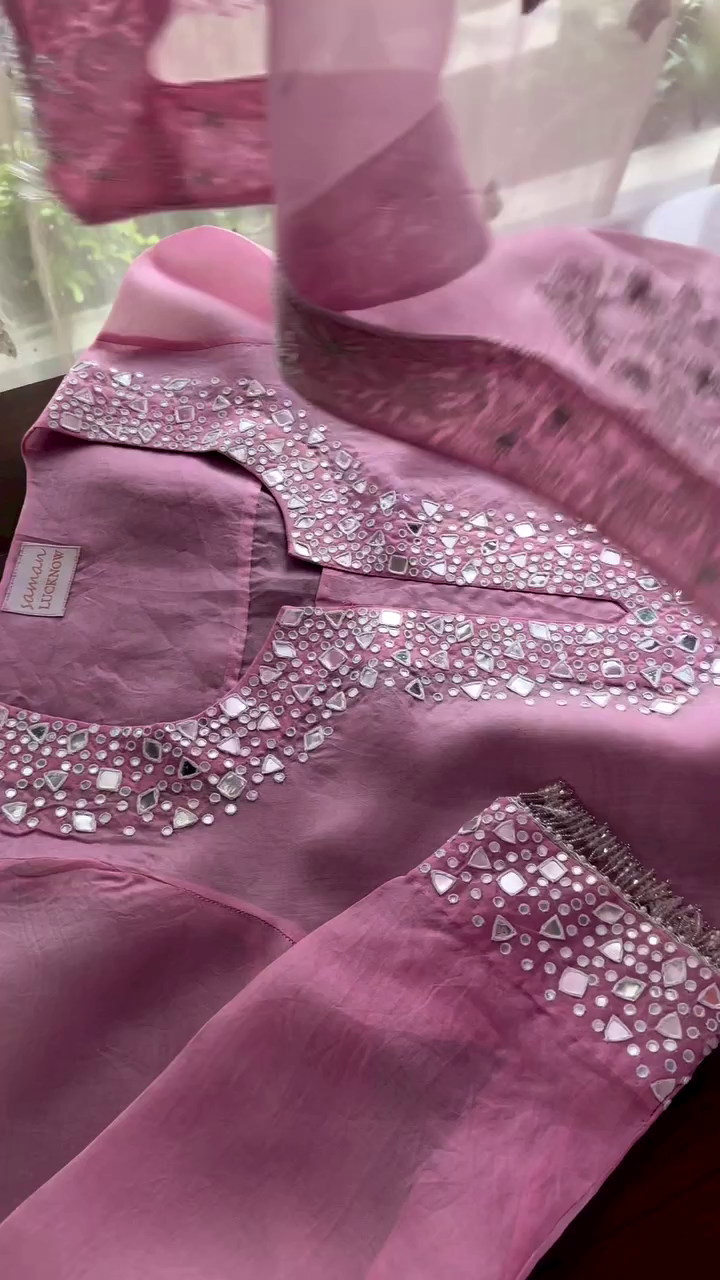 Chic rose pink suit adorned with mirror work around the neckline and cuffs. Paired with a net dupatta featuring detailed floral embroidery and sparkling embellishments.