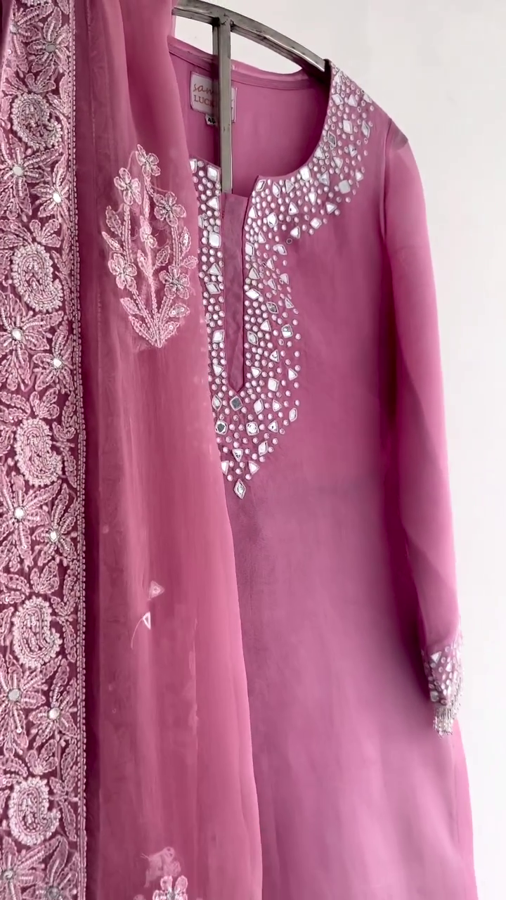 Chic rose pink suit adorned with mirror work around the neckline and cuffs. Paired with a net dupatta featuring detailed floral embroidery and sparkling embellishments.
